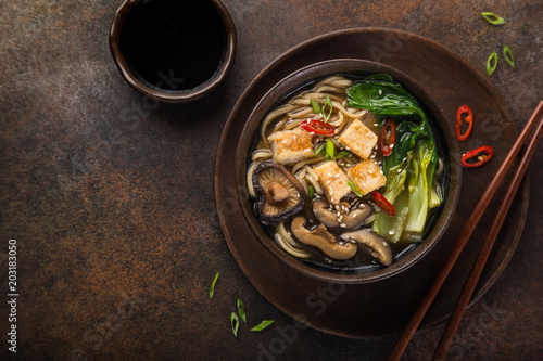 asian vegan noodle soup with tofu cheese, shiitake mushroms and pak choi, dark background