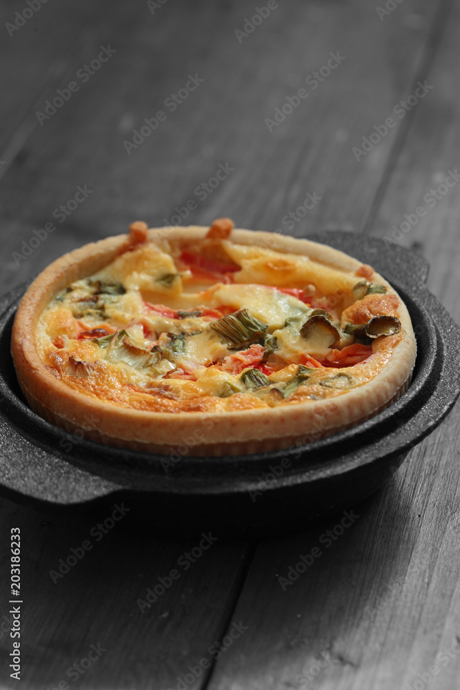 Tomato and spring onion quiche in a cast iron pot dish on a wood background with selective color Tomato and spring onion quiche in a cast iron pot dish on a wood background with selective color