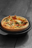 Tomato and spring onion quiche in a cast iron pot dish on a wood background with selective color