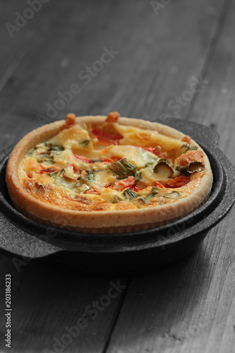 Tomato and spring onion quiche in a cast iron pot dish on a wood background with selective color