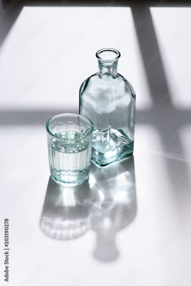 close up view of glass and bottle with water on white surface close up view of glass and bottle with water on white surface
