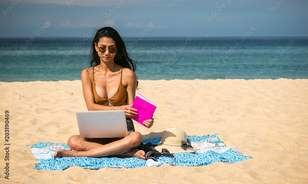 Sexy woman sunbathing and use  laptop , mobile phone on the beach  While relaxing on weekends in travel and holiday concept, Soft focus.