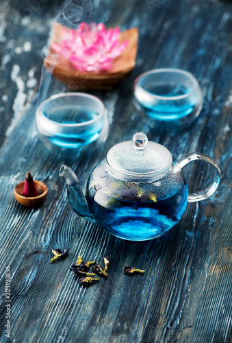 Organic blue tea Anchan, Clitoria, Butterfly Pea in a teapot and a cups and incense on a blue wooden background