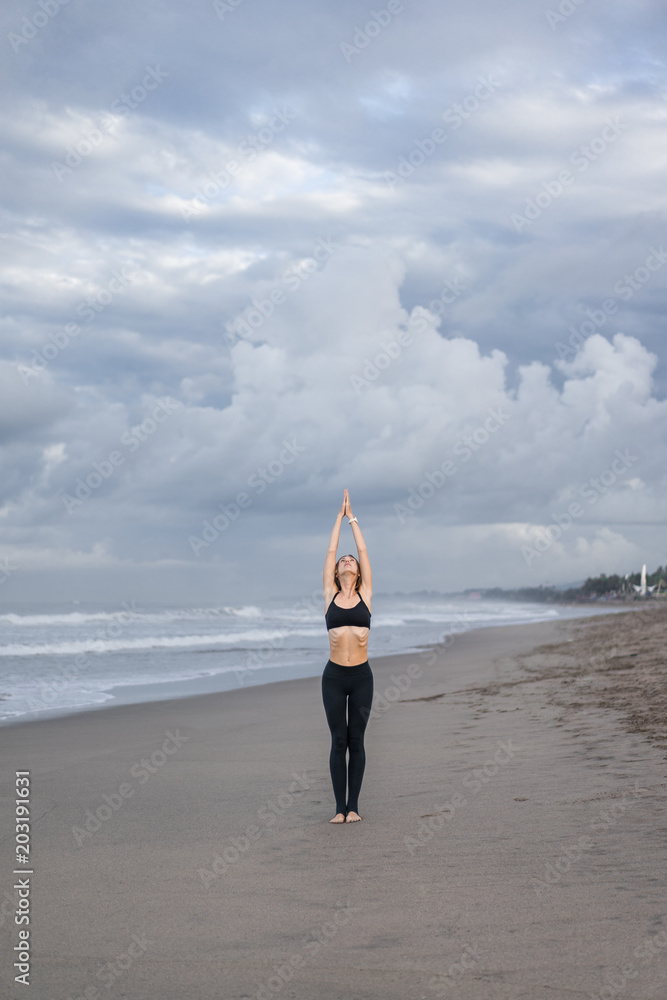 beautiful young woman practicing yoga in Mountain pose (Tadasana) on seashore