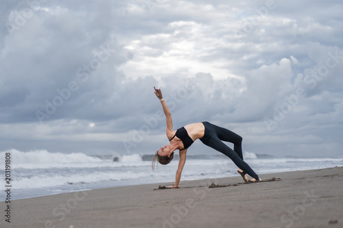 fit young woman practicing yoga on seashore
