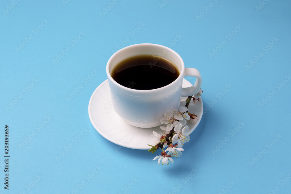 Minimalistic style of the White Cup with Coffee and the Branch of Sakura Blossom on a Blue background Minimalistic style of the White Cup with Coffee and the Branch of Sakura Blossom on a Blue background