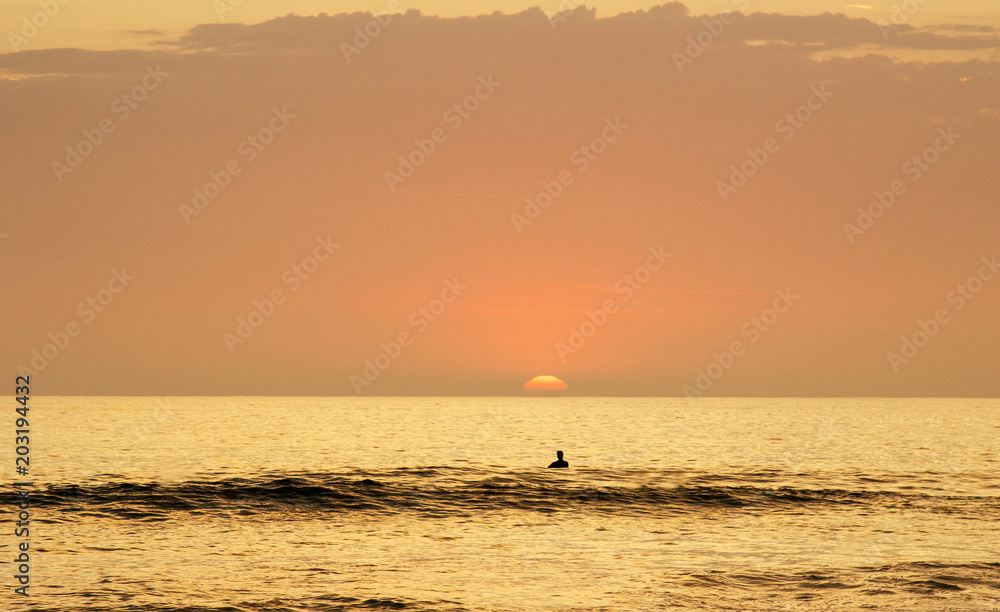 Surfer in the water enjoying the  sun setting into the ocean