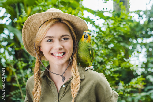 Photography happy young woman in safari suit with parrot on shoulder in jungle