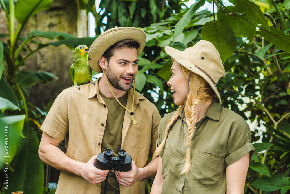 beautiful young couple in safari suits with binoculars hiking together in rainforest