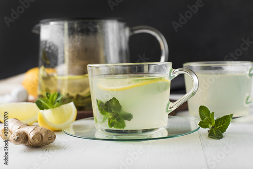 Ginger tea with mint, lemon and honey in a glass cup on a white wooden table