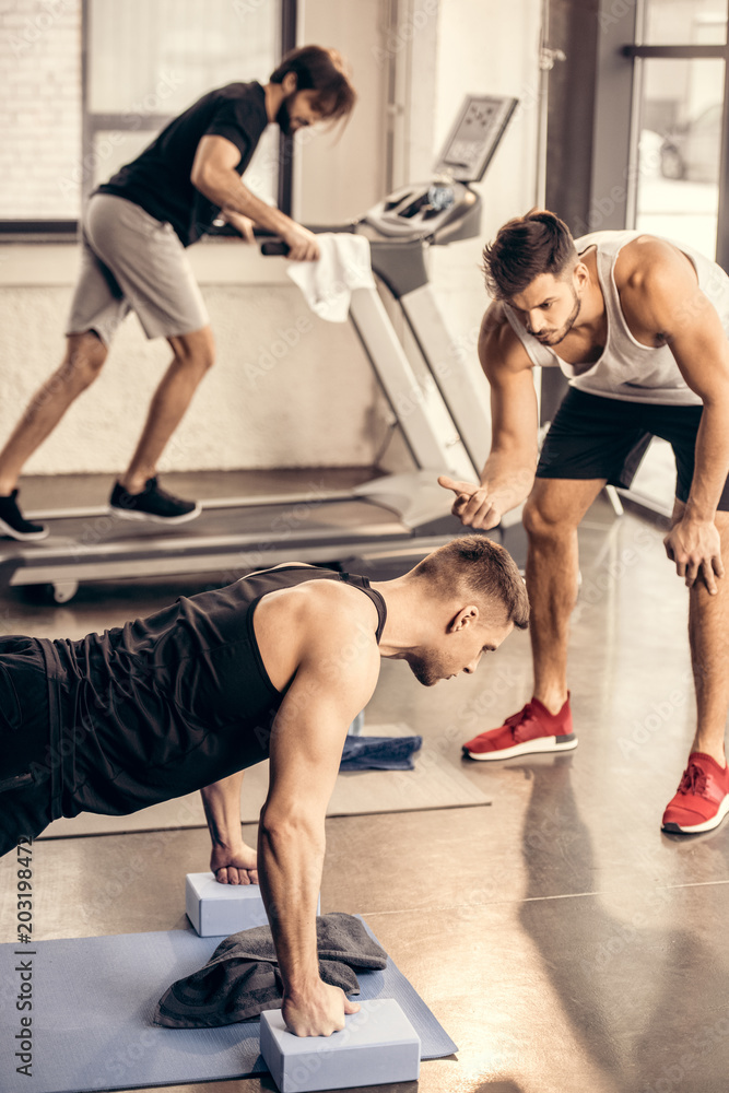 trainer counting while sportsman doing plank on yoga blocks in gym trainer counting while sportsman doing plank on yoga blocks in gym