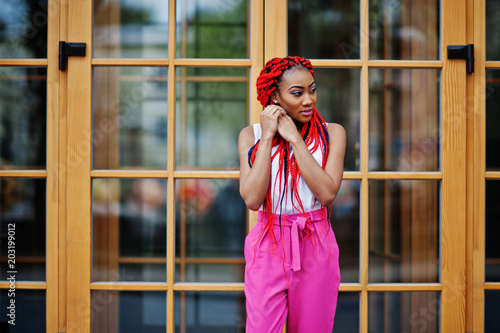 Fashionable african american girl at pink pants and red dreads posed outdoor.