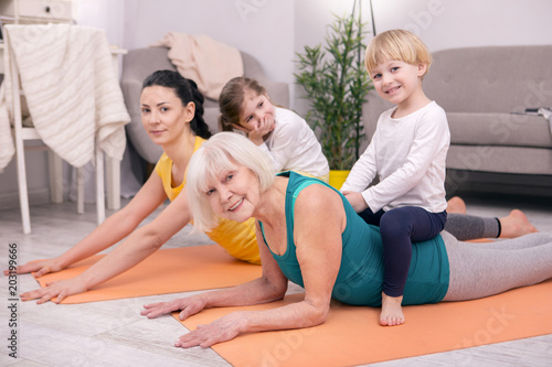 Our leisure. Delighted aged woman sitting on the carpet and exercising with her daughter and grandchildren
