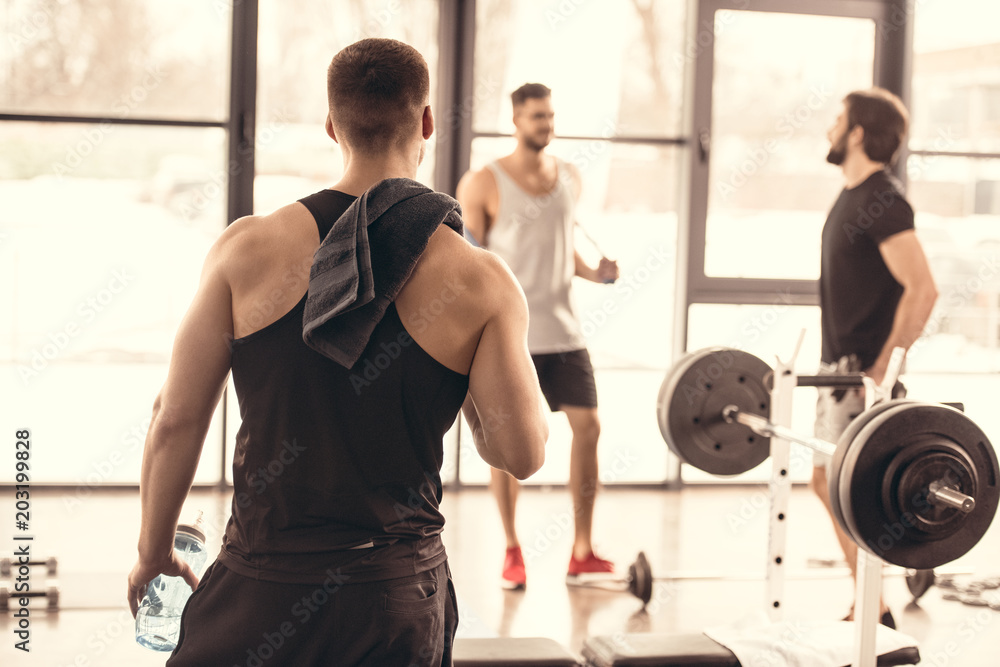 back view of muscular sportsman looking at friends in gym back view of muscular sportsman looking at friends in gym