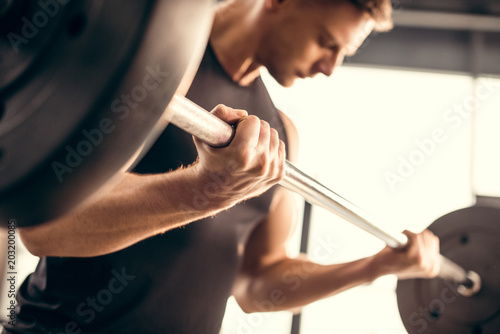 cropped shot of young sportsman lifting barbell in gym