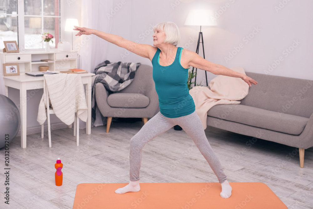Obraz premium Healthy habit. Upbeat elderly woman stretching her arms and doing dynamic exercises during morning calisthenics