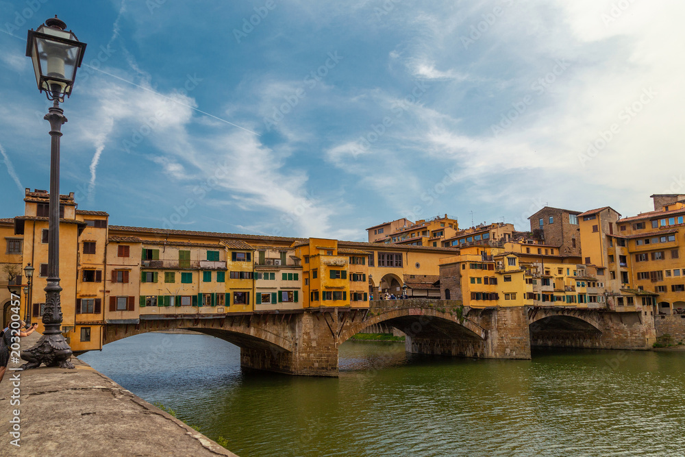 View on The Ponte Vecchio bridge on a sunny day, a medieval stone segmental arch bridge over the Arno River, in Florence, Italy, noted for still having shops built along it
