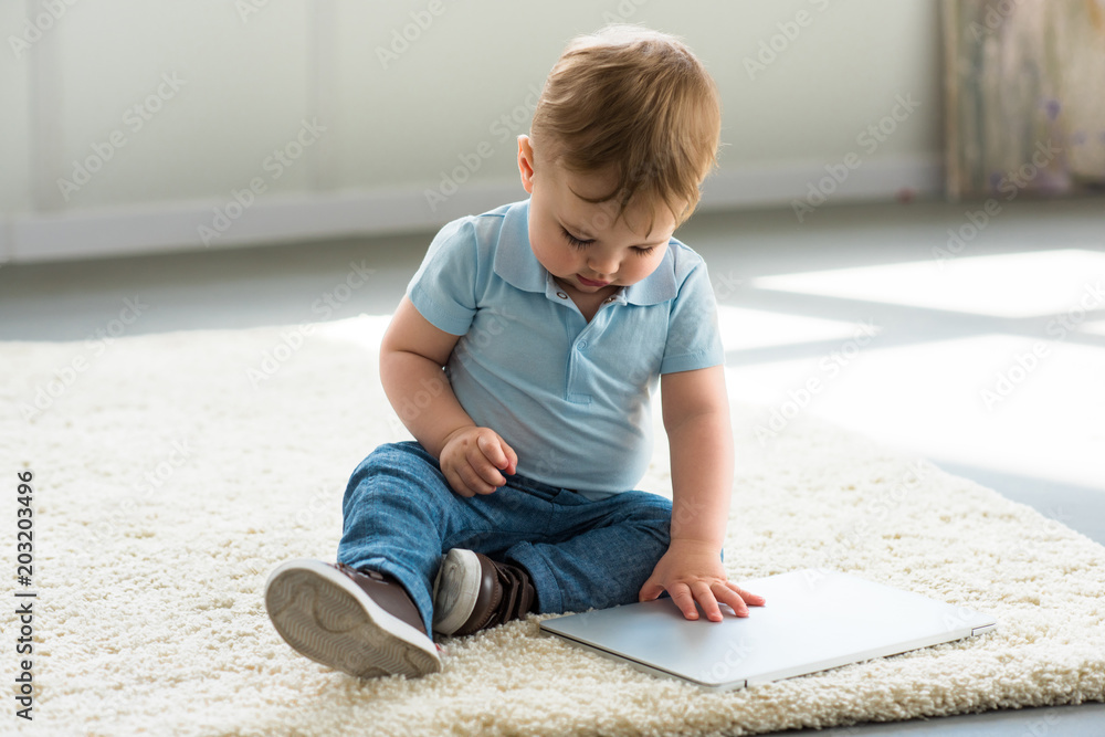 Fototapeta premium little baby boy with laptop sitting on floor at home