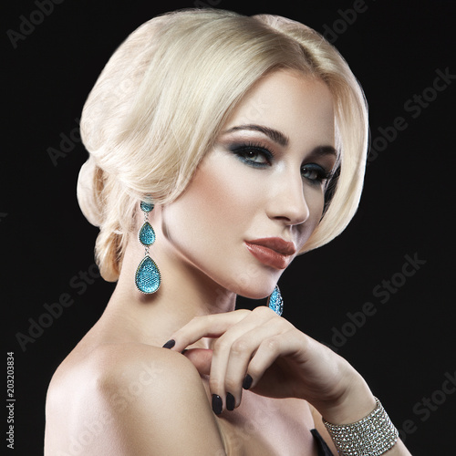 Blonde hair girl with arty makeup, clean skin and jewellery earrings and bracelet over dark studio background