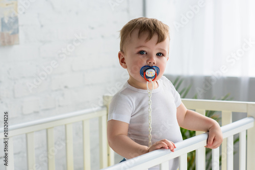 cute little baby boy with pacifier in baby crib looking at camera at home photo