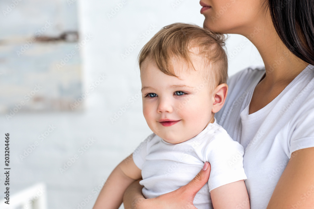 partial view of mother with cute little baby in hands at home partial view of mother with cute little baby in hands at home