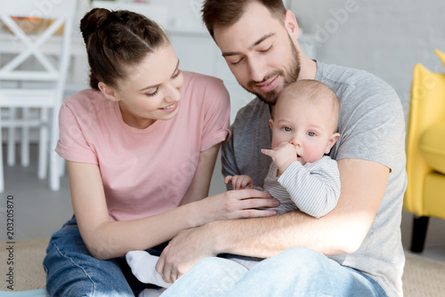 happy young parents with little baby boy sitting on floor