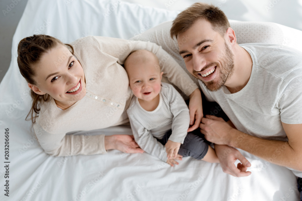 overhead view of happy young parents with infant lying on bed