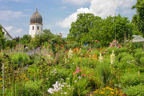 Idylle im Klostergarten des Klosters auf der Insel Frauenchiemsee, mit vielen bunten Blumen im Vordergrund und der Kirchturm im Hintergrund	