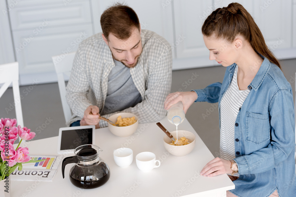 husband and wife having breakfast with corn flakes and coffee in kitchen with digital tablet husband and wife having breakfast with corn flakes and coffee in kitchen with digital tablet