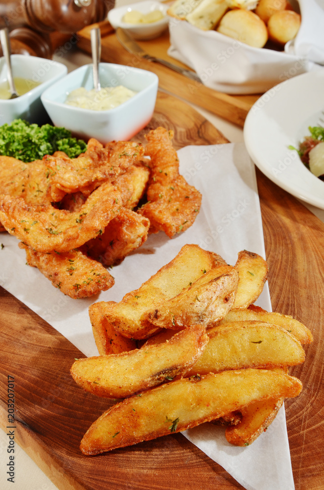Delicious crispy fish with chips and sauce on wooden plate Delicious crispy fish with chips and sauce on wooden plate