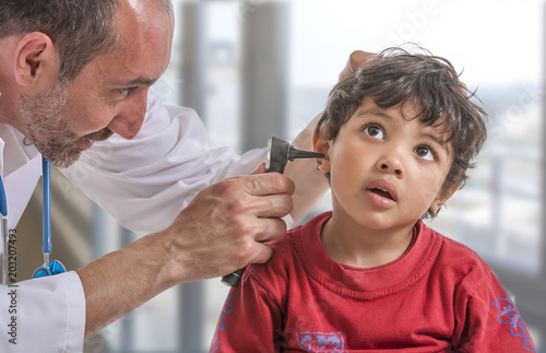 A pediatrician examining his boy patient's ear at doctor's office photo