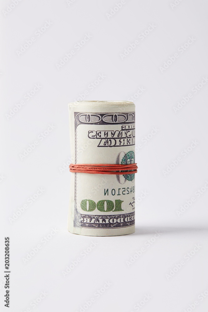Roll of dollars tied with rubber band on white surface Roll of dollars tied with rubber band on white surface