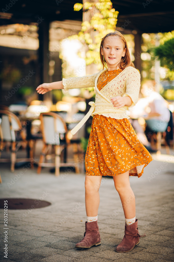 Naklejka premium Outdoor fashion portrait of cute preteen girl, wearing brown dress and yellow knitted jacket