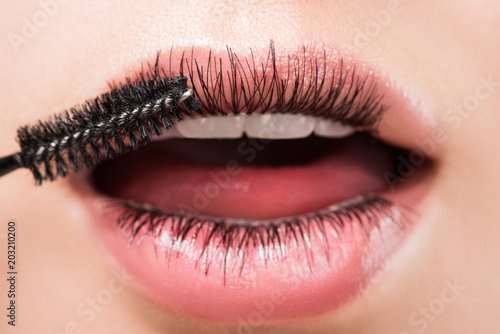 cropped image of woman applying black mascara on eyelashes in mouth isolated on white