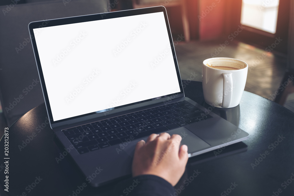 Mockup image of businessman using and typing on laptop with blank white screen and coffee cup on table in cafe Mockup image of businessman using and typing on laptop with blank white screen and coffee cup on table in cafe