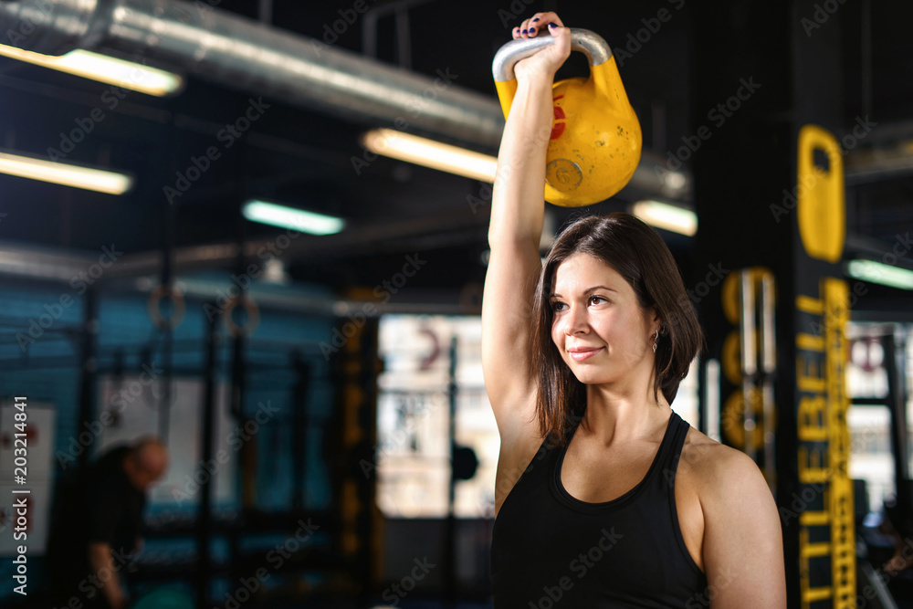 Fitness woman doing a weight training by lifting kettlebell. Muscular