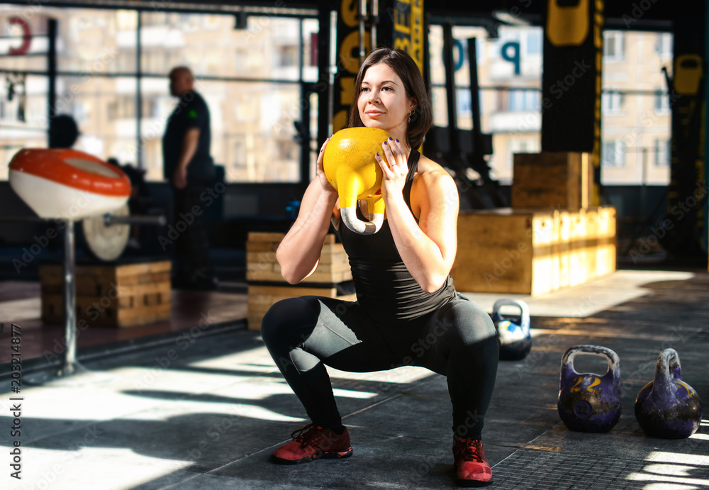 Fitness woman a weight training by lifting kettlebell. Muscular fitness woman, holds up a yellow kettlebell crossfit the gym. Fitness woman in the gym. Crossfit woman. Healthy lifestyle Stock Photo