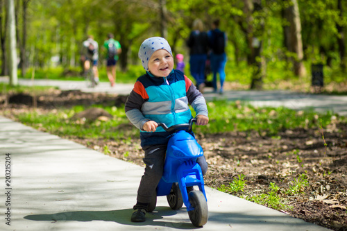 Little boy riding toy motorbike in green sunny park. Active childhood