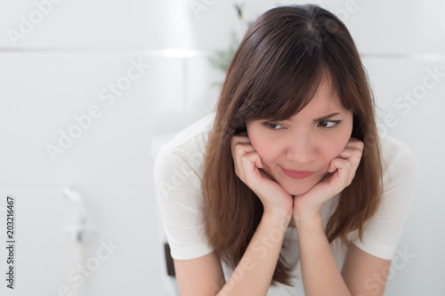 upset woman in toilet by diarrhea, constipation, hemorrhoids, piles; portrait of woman hard pushing in toilet or wc from diarrhea, constipation, food poisoning, hemorrhoids; asian adult woman model