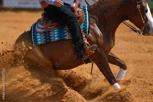 The rider on a reining horse slides to a stop in the red clay an arena.