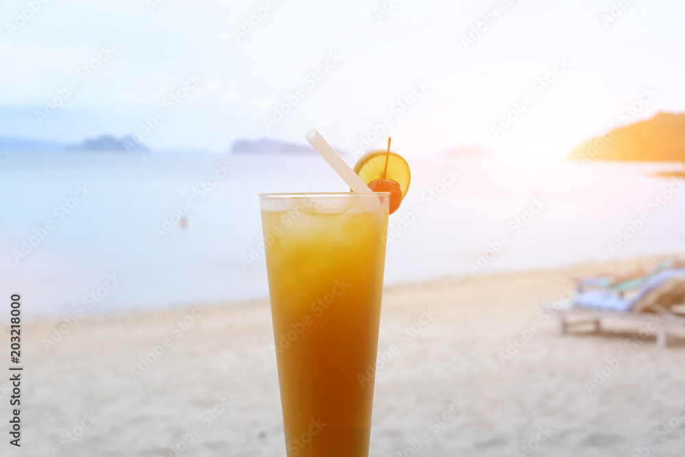 Obraz premium Fresh orange juice at the beach, Glass of orange juice on the sandy beach with sea in background