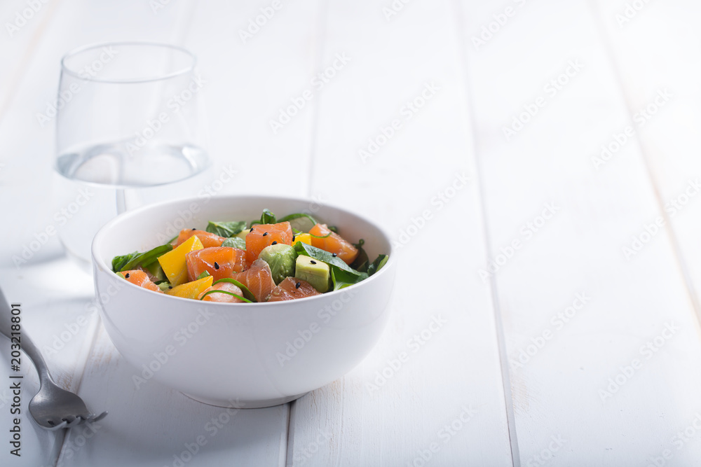 Hawaiian Poke salad with salmon, avocado and vegetables in a bowl on a white wooden rustic background with copy space, vegetables and a fork Hawaiian Poke salad with salmon, avocado and vegetables in a bowl on a white wooden rustic background with copy space, vegetables and a fork