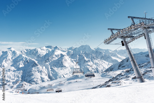Chairlift in the Alpine ski resort. Support and empty seats. Snow-capped mountain peaks on a Sunny day