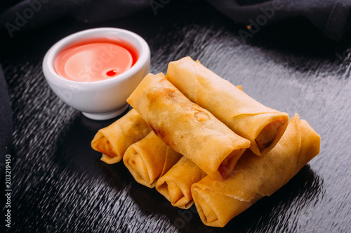 lumpias with sweet sauce on a black background