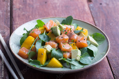 Hawaiian Poke salad with salmon, avocado and vegetables on the plate on a brown wooden rustic background
