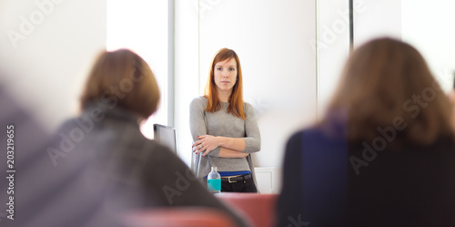 Confident smart female doctoral student presenting his study work in front of professors's choir, defending his thesis. Doctoral thesis defense on faculty.