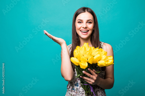 Beautiful excited girl in the dress with flowers tulips in hands on a blue background photo
