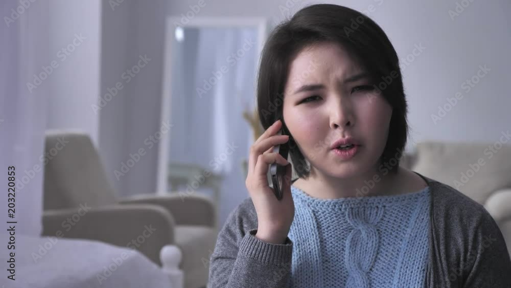 Young sad Asian girl speaks aggressively on the phone using smartphone, portrait, drunk husband in background 50 fps Young sad Asian girl speaks aggressively on the phone using smartphone, portrait, drunk husband in background 50 fps