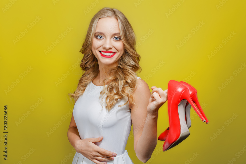 Another picture of a girl holding red shoes with high heels in one hand and  holding