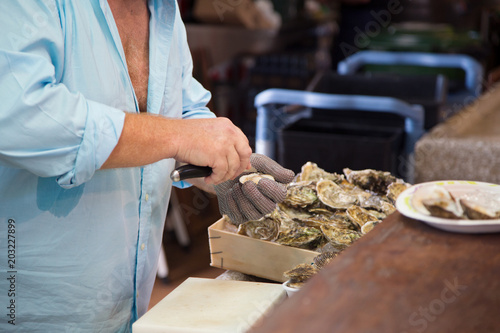 Shucking fresh oysters with an oyster knife on a fish market